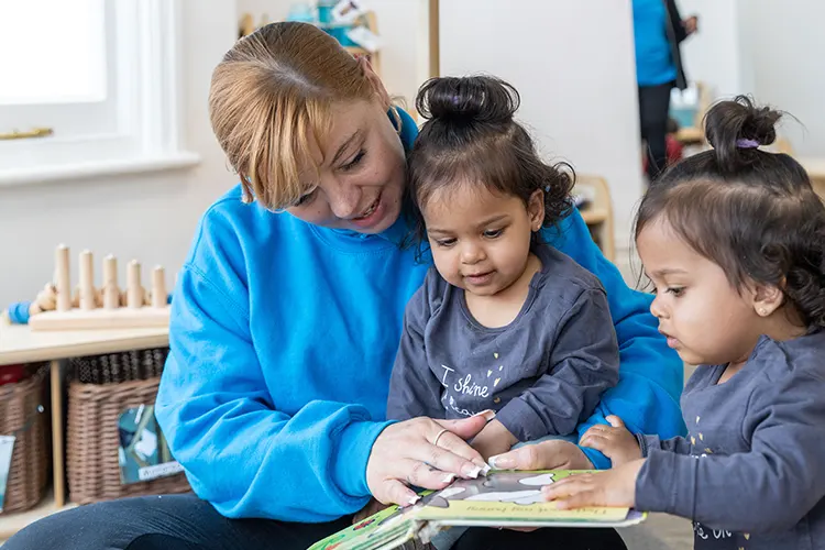 Staff member sat with nursery children as they read a book